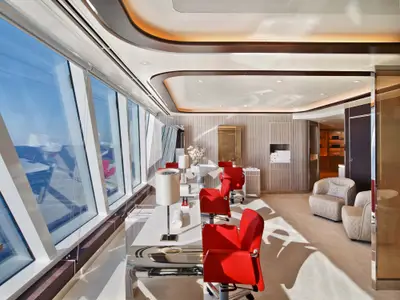 Friseursalon und Spa-Bereich an Bord der Seabourn Encore mit roten Sesseln, Maniküretisch und großen Panoramafenstern zum Meer.