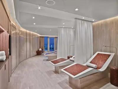 Moderne, beheizte Steinliegen mit Mosaikfliesen und weißen Vorhängen im Wellnessbereich an Bord der Seabourn Encore.