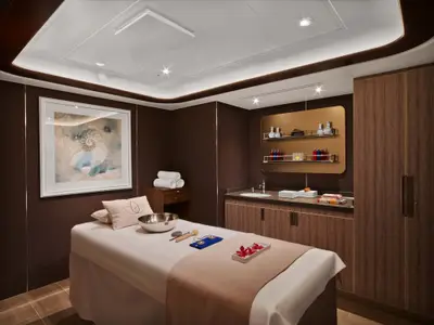 Ein eleganter Spa-Behandlungsraum an Bord der Seabourn Encore mit einer Massageliege, Klangschale und edler Holzverkleidung.