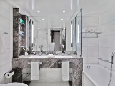 Blick auf das elegante Doppelwaschbecken mit Marmor-Armaturen und Badewanne an Bord der Seabourn Encore.