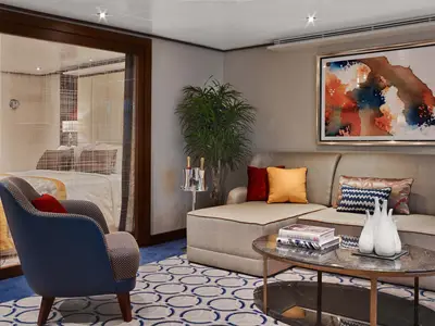 Einblick in eine luxuriöse Suite an Bord der Seabourn Encore mit gemütlichem Sofa, Couchtisch und Blick auf das Doppelbett.