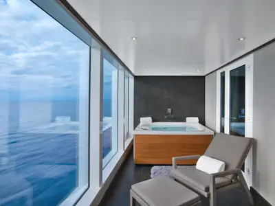 Luxuriöser Whirlpool und eine Liege im verglasten Balkon der Wintergarden Suite an Bord der Seabourn Encore mit Blick auf das blaue Meer.