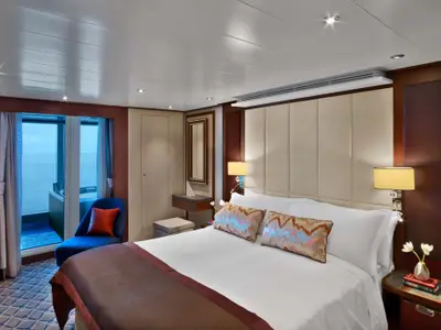 Das luxuriöse Schlafzimmer einer Suite an Bord der Seabourn Encore mit großem Doppelbett, Sessel und Blick auf den Balkon mit Meerblick.