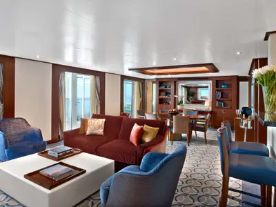Die elegante Wintergarden Suite an Bord der Seabourn Encore mit einem großen roten Sofa, blauen Sesseln und einem Esstisch.
