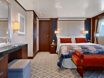 Eine elegante Suite an Bord der Seabourn Encore mit einem großen Doppelbett, stilvollen Holzmöbeln und gemütlicher Beleuchtung.