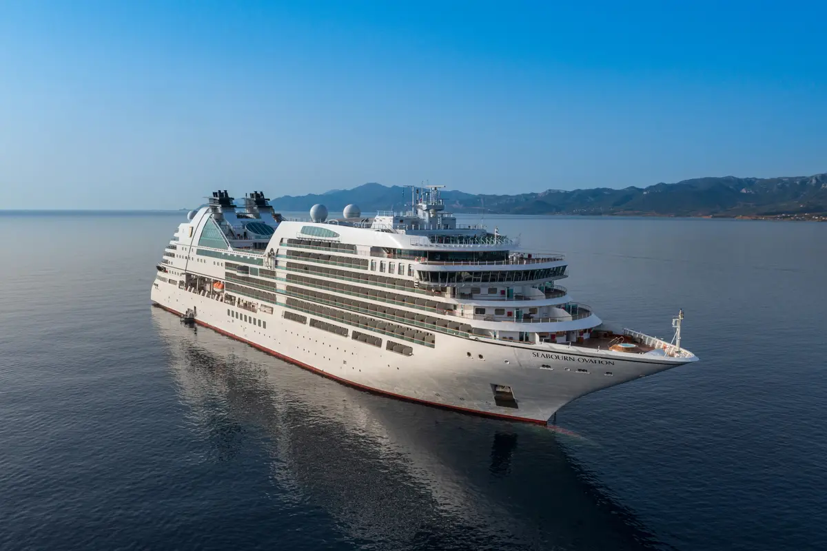 Außenansicht des Luxusschiffs Seabourn Ovation auf dem ruhigen, blauen Meer vor einer bergigen Kulisse.