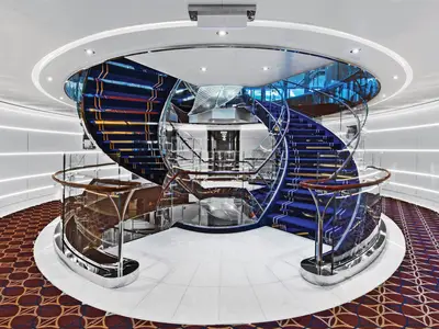 Die geschwungene, blau beleuchtete Treppe mit gläsernem Geländer im Atrium an Bord der Seabourn Ovation.