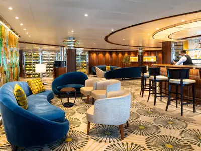 Gemütliche Bar-Lounge an Bord der Seabourn Ovation mit blauen Sofas, einer Holztheke und stilvollen Weinschränken.