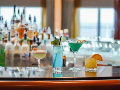 Vier verschiedene, farbenfrohe Cocktails stehen auf der glänzenden Theke der Observation Bar an Bord der Seabourn Ovation.