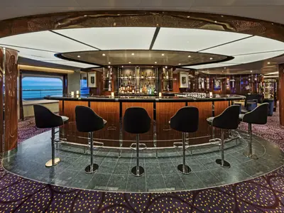 Die elegante Bar 'The Club' an Bord der Seabourn Ovation mit modernen Barhockern, einer geschwungenen Theke und Blick aufs Meer.