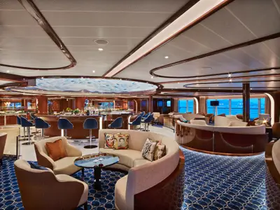 Blick in die elegante Observation Bar an Bord der Seabourn Ovation mit geschwungenen Sofas, blauen Barhockern und Meerblick.