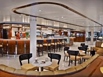 Die elegante Kaffeebar an Bord der Seabourn Ovation mit geschwungener Holztheke, Barhockern, Tischen und feinen Sitzgelegenheiten im modernen Design.