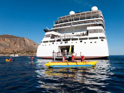 Gäste beim Wassersport mit Bananenboot und Paddleboards direkt hinter dem Heck der Seabourn Ovation.