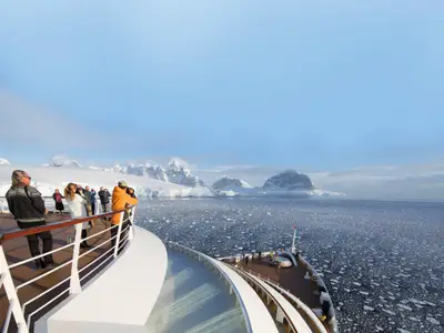 Blick vom Deck der Seabourn Ovation auf Passagiere, die die schneebedeckten Berge und Eisschollen der Antarktis fotografieren.