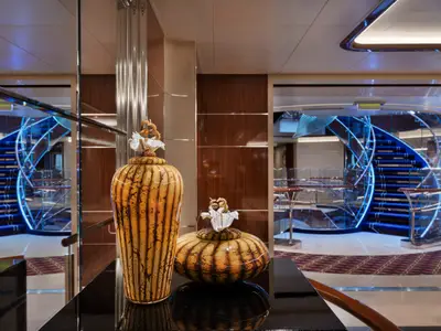 Elegante, kunstvoll gemusterte Vasen im Vordergrund vor einer blau beleuchteten Wendeltreppe an Bord der Seabourn Ovation.