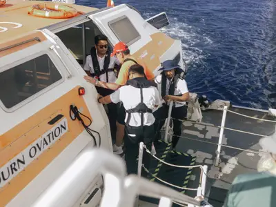 Crew-Mitglieder unterstützen einen Passagier beim sicheren Einstieg in das Tenderboot der Seabourn Ovation auf dem Meer.