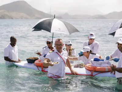 Crew-Mitglieder der Seabourn Ovation servieren Kaviar im türkisblauen Meer auf einem schwimmenden Tablett.