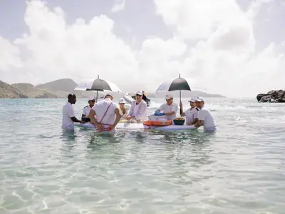 Die Crew der Seabourn Ovation serviert Champagner und Kaviar auf einem schwimmenden Board im klaren, flachen Meer.