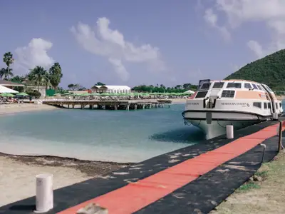 Das Tenderboot der Seabourn Ovation liegt an einem Steg vor einem tropischen Sandstrand mit Sonnenschirmen in der Karibik.