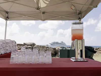 Erfrischungsgetränke und Handtücher unter einem Zelt, im Hintergrund die Seabourn Ovation auf dem Meer vor St. Kitts.