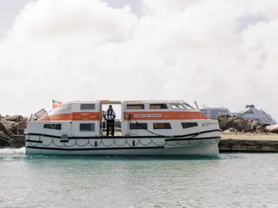 Ein Tenderboot der Seabourn Ovation liegt im Hafenbecken vor einer felsigen Kulisse, während ein Crewmitglied an Bord steht.