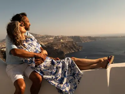 Ein Paar genießt den Ausblick auf das Meer und die Seabourn Ovation von einer weißen Mauer in Santorini.