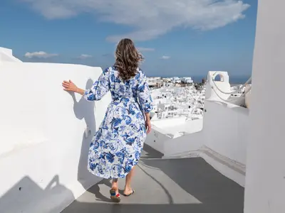 Eine Frau im blau-weißen Kleid blickt bei einem Landausflug der Seabourn Ovation auf ein griechisches Dorf.