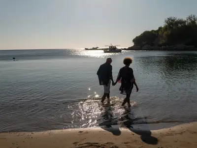 Ein Paar geht Hand in Hand im seichten Meerwasser am Strand spazieren während eines Landausflugs der Seabourn Ovation.