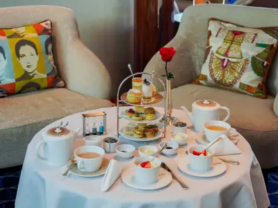 Ein reich gedeckter Tisch für den Afternoon Tea an Bord der Seabourn Ovation mit Teekannen, Etagere und einer roten Rose.