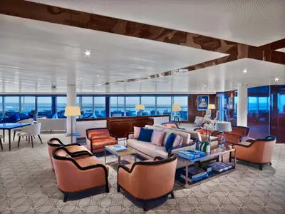 Sitzbereich mit bequemen Clubsesseln, Sofas und großen Panoramafenstern in einer Lounge an Bord der Seabourn Ovation.