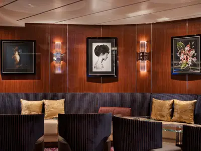 Eine stilvoll eingerichtete Lounge an Bord der Seabourn Ovation mit edlen Holzpaneelen, Kunstbildern und gemütlichen Sofas.