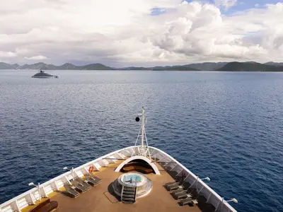 Blick vom Bug der Seabourn Ovation mit einem Whirlpool auf dem Holzdeck auf das blaue karibische Meer und grüne Inseln im Hintergrund.