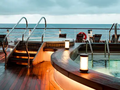 Ein beleuchteter Whirlpool und Poolbereich mit Holzdeck am Abend an Bord der Seabourn Ovation.