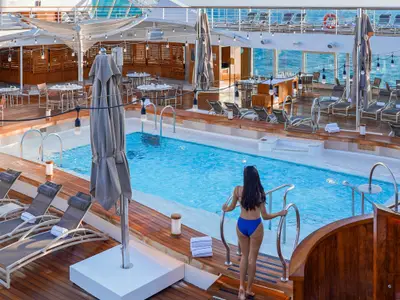 Eine Frau im blauen Bikini blickt auf den einladenden Pool auf dem Deck an Bord der Seabourn Ovation.