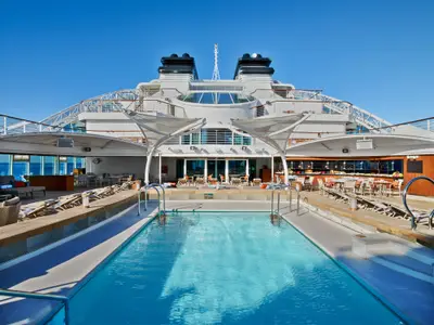 Blick auf den von Liegestühlen umgebenen Swimmingpool auf dem Sonnendeck an Bord der Seabourn Ovation bei strahlendem Sonnenschein.