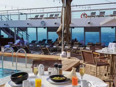 Ein elegant gedeckter Tisch mit Champagnergläsern auf dem Sonnendeck der Seabourn Ovation am Pool.