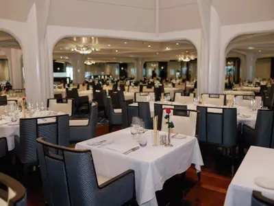 Fein gedeckte Tische mit Gläsern und einer roten Rose im Restaurant an Bord der Seabourn Ovation.