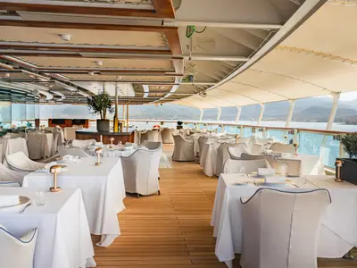 Elegant eingedeckte Tische im Restaurantbereich an Bord der Seabourn Ovation mit freiem Blick auf das Meer und die Küste.