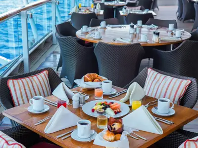 Ein reich gedeckter Frühstückstisch mit Obst und Kaffee auf dem Außendeck der Seabourn Ovation mit Blick auf das Meer.