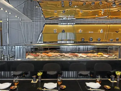 Blick auf den eleganten Sushi-Tresen mit frischem Fisch auf Eis und goldfarbenem Hintergrund an Bord der Seabourn Ovation.