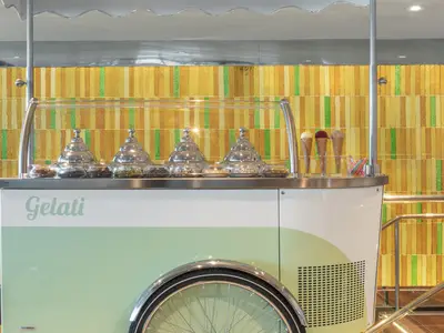 Ein hellgrüner Eiswagen mit glänzenden Silberhauben an Bord der Seabourn Ovation vor einer bunt gefliesten Wand.