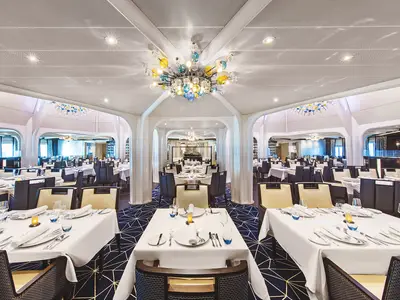 Elegantes Restaurant an Bord der Seabourn Ovation mit weiß eingedeckten Tischen und einem farbigen Glaslüster.