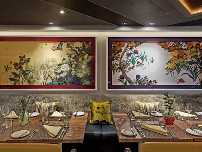 Eingedeckte Tische mit feinem Geschirr und bunten, floralen Wandbildern im Restaurant an Bord der Seabourn Ovation.