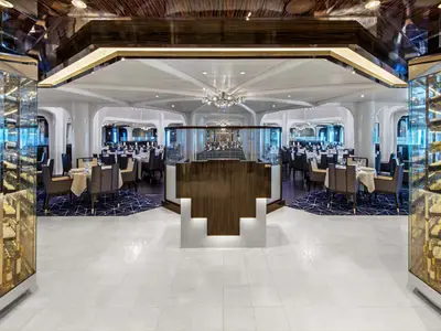 Elegantes Restaurant an Bord der Seabourn Ovation mit weißem Fliesenboden, dunklen Tischen und beleuchteten Weinregalen an den Seiten.