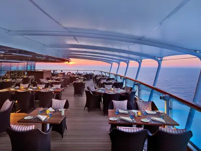 Gedeckte Tische auf dem Außendeck des Restaurants an Bord der Seabourn Ovation mit Blick auf das weite Meer bei Sonnenuntergang.