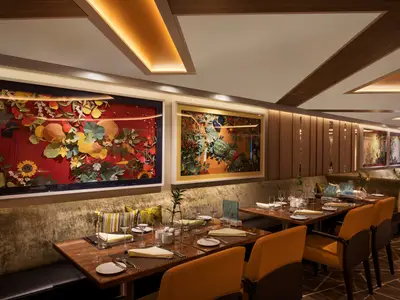 Elegant eingedeckte Tische und gelbe Stühle in einem gemütlichen Restaurant an Bord der Seabourn Ovation, dekoriert mit farbenfroher Kunst.