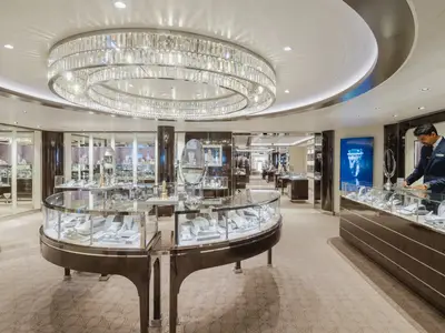 Ein edler Juwelierladen an Bord der Seabourn Ovation mit gläsernen Vitrinen, einem prachtvollen Kristallkronleuchter und einem Verkäufer.