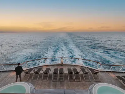 Ein Mann steht am Heck der Seabourn Ovation und blickt beim Sonnenuntergang auf die Heckwelle im Meer.