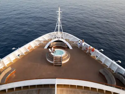 Blick aus der Vogelperspektive auf das hölzerne Bug-Deck an Bord der Seabourn Ovation mit einem runden Whirlpool und Gästen.