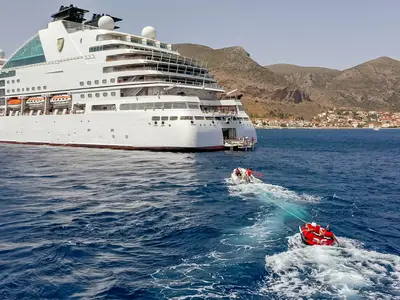 Blick auf das Heck der Seabourn Ovation vor bergiger Kulisse, während ein Beiboot Urlauber auf einem Reifen zieht.